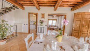 Zona pranzo con tavolo imbandito per quattro persone, una scala e vista sul soggiorno.