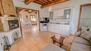 Un'ampia zona giorno con camino, un divano, un tavolo da pranzo e una cucina con mobili bianchi.
