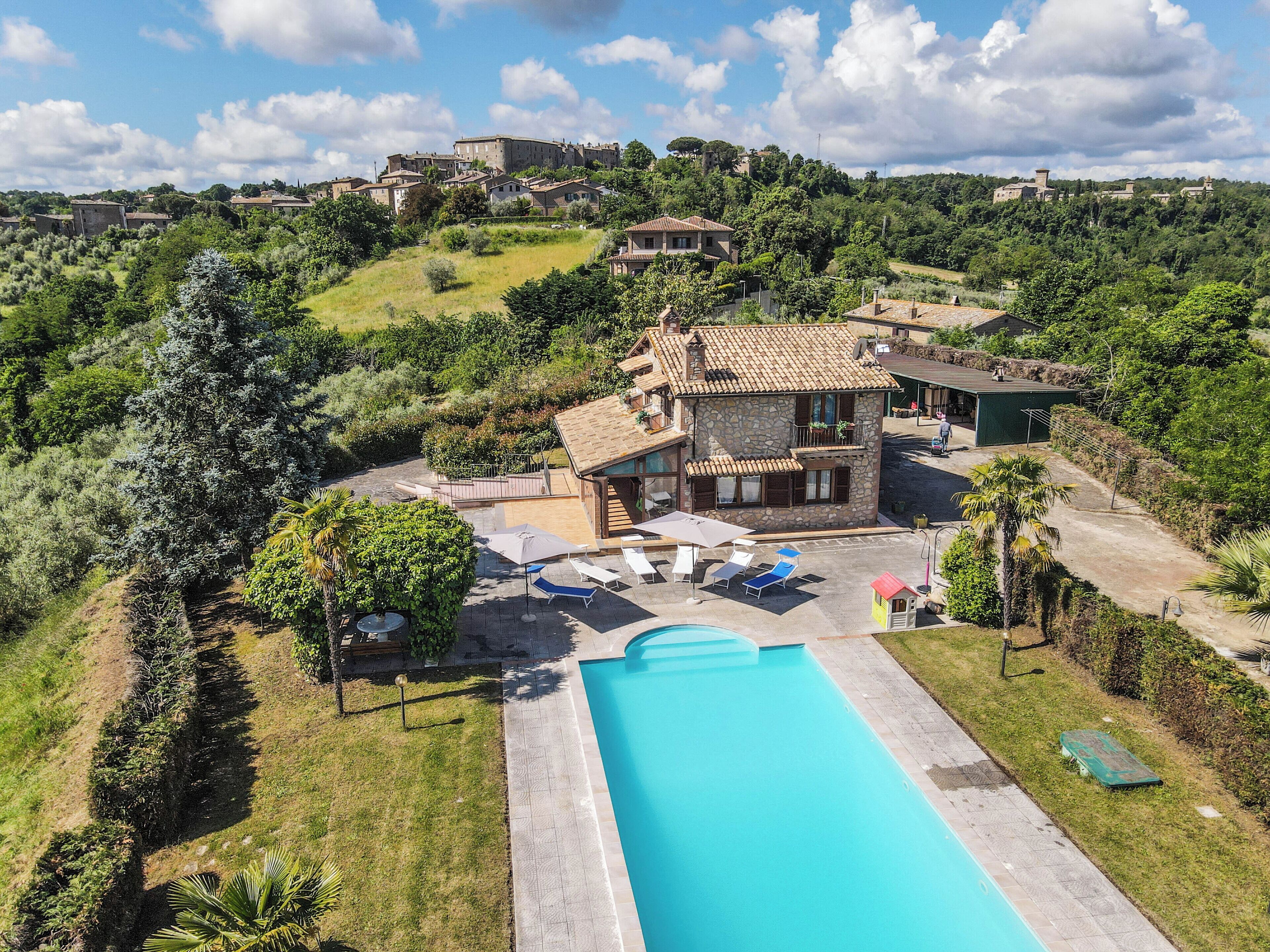 A villa with a swimming pool, surrounded by lush greenery and a hilly landscape.
