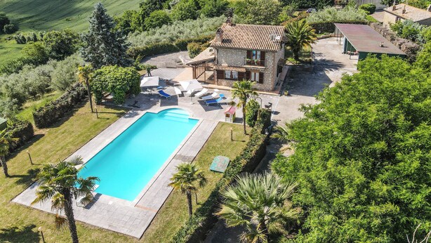 Una villa in pietra con piscina, immersa nel verde e circondata da un paesaggio collinare.