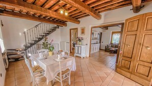 Un'ampia sala da pranzo con una scala in legno, pavimento in piastrelle bianche e soffitto in legno.