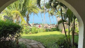 Ein tropischer Garten, der zu einem Strand mit Palmen und Reetdachschirmen führt.