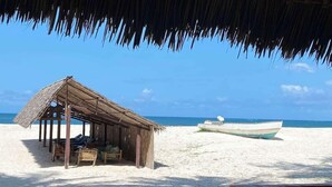 Eine Strandhütte mit einem Reetdach, ein Boot und ein Sandstrand.