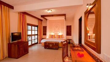 A hotel room with a bed, a television, a wooden table, and a large mirror.