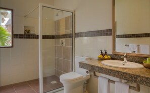 A modern bathroom with a glass-enclosed shower, a white toilet, a sink with a granite countertop, and a mirror above the sink. - Neptune Village Beach Resort & Spa (Diani Beach)