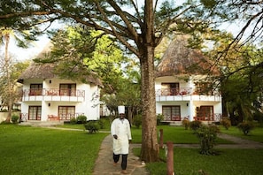 A building with a thatched roof, a central walkway, and a person in chef attire. - Neptune Village Beach Resort & Spa (Diani Beach)