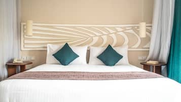 Een hotelkamer met een groot bed, twee kussens, een hoofdbord met bladmotief, nachtkastjes en een wandlamp.