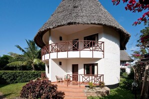 A thatched-roof building with a balcony, surrounded by greenery. - Neptune Village Beach Resort & Spa (Diani Beach)