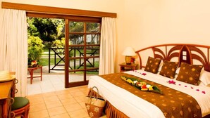 A bedroom with a bed, a nightstand, a lamp, a chair, a table, a window, and a view of the outdoors. - Neptune Village Beach Resort & Spa (Diani Beach)