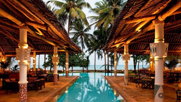 A pool area with a clear view of the ocean, surrounded by palm trees and covered with a thatched roof. - Neptune Village Beach Resort & Spa (Diani Beach)