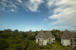 A row of thatched-roof cottages with a clear view of the surrounding lush greenery. - Neptune Village Beach Resort & Spa (Diani Beach)