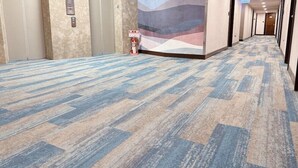 Un pasillo de hotel con piso alfombrado, un extintor y una pared con diseño geométrico.