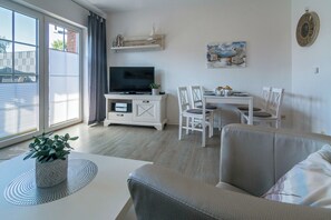A modern living room with a flat-screen TV, a dining table, and a sofa. - Your Getaway in Norddeich: A Quiet Location, a Garden, and an Allergy-Friendly Apartment (Norden)