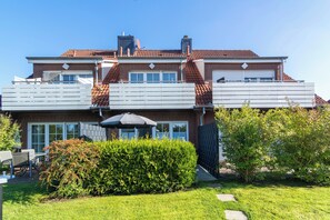A two-story house with a balcony, a patio with a table and chairs, and a well-maintained garden. - Your Getaway in Norddeich: A Quiet Location, a Garden, and an Allergy-Friendly Apartment (Norden)