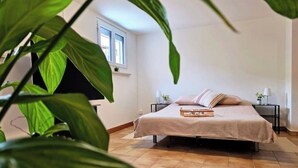 Ein Schlafzimmer mit einem Bett, Nachttischen, einem Fenster und einer Pflanze.