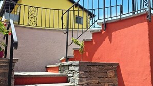 Eine Treppe mit Steinstufen führt zu einem Balkon mit einer gelben Wand und einem schwarzen Geländer.