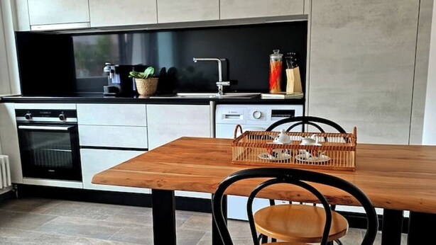 Eine moderne Küche mit einem Holzespeisetisch und Stühlen, einem eingebauten Backofen und einem Geschirrspüler.