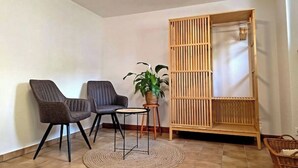 Ein Zimmer mit zwei Stühlen, einem kleinen Tisch, einer Topfpflanze und einem Holzschrank.