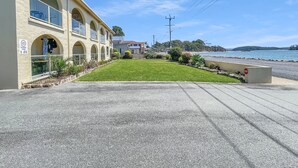 A beachfront building with a shared parking zone sign, a grassy lawn, and a stop sign near the road. - Beachside Apartment Overlooking Casey’s Beach (Batehaven)