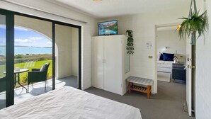 A bedroom with a bed, a small bench, a wardrobe, and a television. There is a balcony with a view of the sea. - Beachside Apartment Overlooking Casey’s Beach (Batehaven)