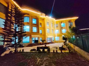 A multi-story building with a yellow facade, large windows, and a well-lit entrance area. - Park In By Jolly Plaza (Reasi)