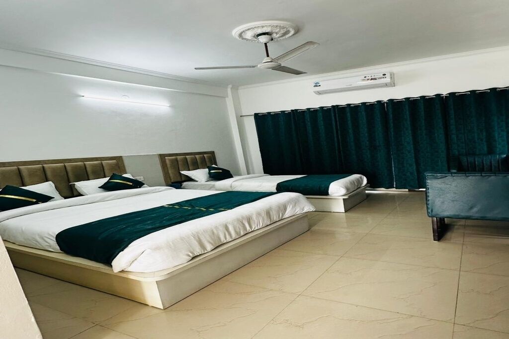 Habitación de hotel con dos camas, ventilador de techo, aire acondicionado y cortina oscura.