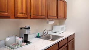 A kitchen with wooden cabinets, a coffee maker, a microwave, a sink, and a tray with coffee cups and a bottle. - The Southernmost Inn - Adult Exclusive (Key West)