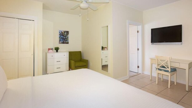 A bedroom with a bed, a desk, a chair, a television, a wardrobe, and a ceiling fan. - The Southernmost Inn - Adult Exclusive (Key West)