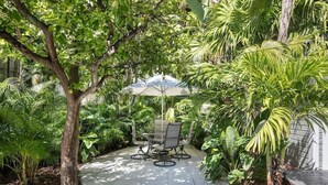 A patio with a table and chairs, surrounded by lush greenery and a tree. - The Southernmost Inn - Adult Exclusive (Key West)