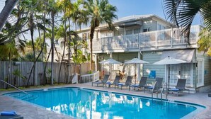A swimming pool with lounge chairs and umbrellas, surrounded by palm trees and a building with a balcony. - The Southernmost Inn - Adult Exclusive (Key West)