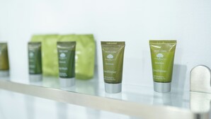 Una fila de botellas verdes con la etiqueta 'Basic Earth Botanicals Conditioner' sobre una estantería.