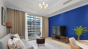 Un soggiorno moderno con un divano grigio, un tavolino rotondo, una televisione e una parete di colore blu.