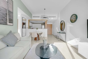 A modern living room with a white sofa, a coffee table, and a dining area with a white table and chairs. - Perfect Getaway in Downtown l Near Dubai Mall (Downtown)