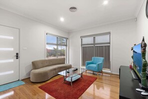 Una sala de estar moderna con un sofá color crema, un sillón azul, una mesa de centro de vidrio y un tapete rojo.