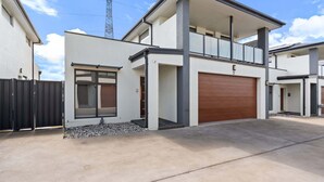 A modern two-story house with a garage, a balcony, and a large window. - Family-Friendly 4-Bed Home with Courtyard (Holt)