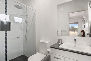 Un baño moderno con ducha de vidrio, inodoro y lavamanos con espejo.