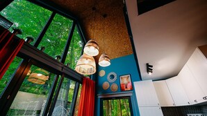 A room with large windows, a hanging light fixture, and a view of greenery outside.