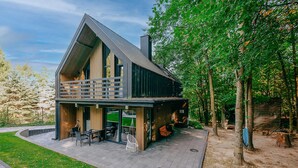 A modern house with a large balcony, a covered patio, and a view of a forested area.