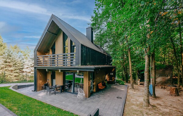 Ein modernes Haus mit einem großen Balkon, einer überdachten Terrasse und Blick auf ein bewaldetes Gebiet.
