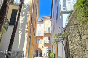 Uma rua estreita com edifícios de ambos os lados, com varandas e um muro de pedra à direita.