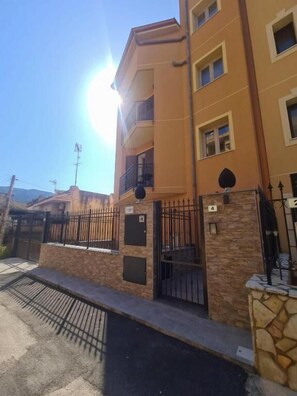 A multi-story residential building with a gated entrance, stone wall, and a clear sky. - Aphrodite's apartment at Aspra (BAGHERIA)