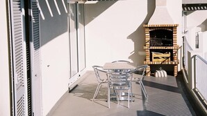 A balcony with a glass table and chairs, a barbecue grill, and a sliding door. - Paraiso Dourado (Porto Santo)