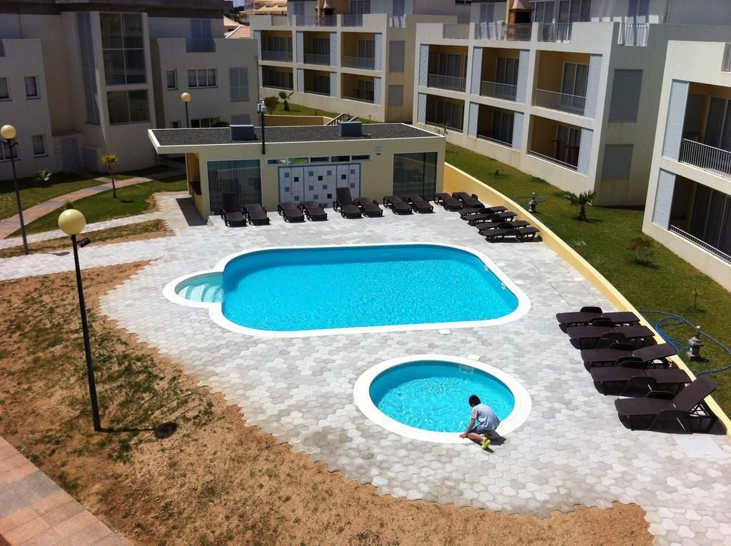 A swimming pool with lounge chairs, a small circular pool, and a building with balconies.
