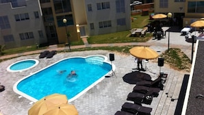 A swimming pool with lounge chairs and umbrellas, surrounded by a paved area with buildings in the background. - Paraiso Dourado (Porto Santo)