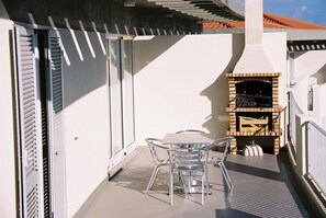 Een balkon met een glazen tafel en stoelen, een barbecue en een schuifdeur.