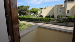Vue depuis un balcon doté d’une bordure en béton et d’un cadre de porte en bois. Au fond, on aperçoit des bâtiments à l’architecture moderne, une route et quelques espaces verts.