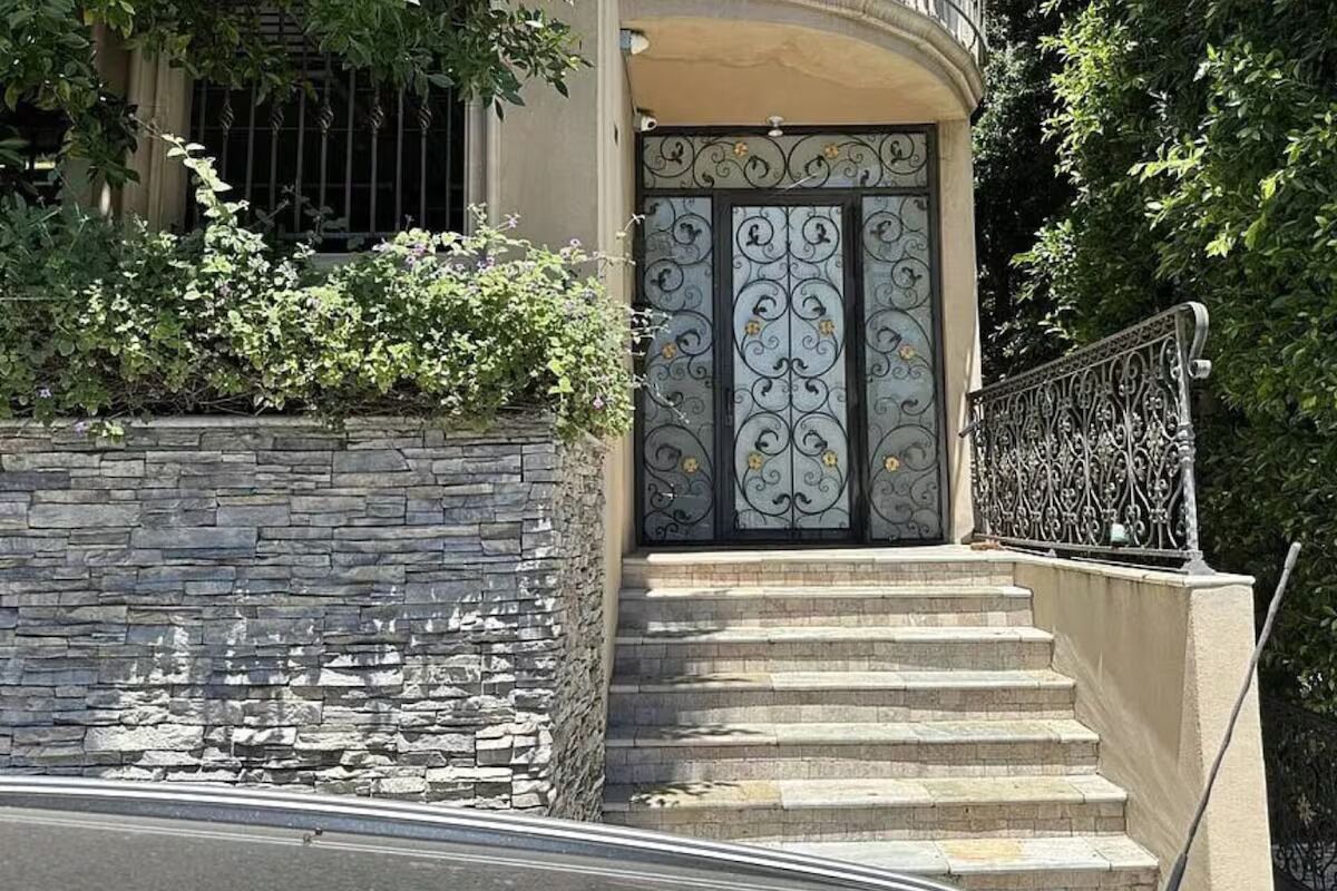 Un muro de piedra con una verja metálica y escalones que llevan a un edificio.