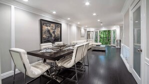 Une salle à manger moderne avec une table en bois foncé, des chaises à revêtement blanc et un grand tableau abstrait accroché au mur.