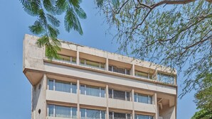 A multi-story building with a flat facade, a sign reading "Roger Hotel," and a covered entrance area with potted plants. - Regent Hotel Andheri (Mumbai)