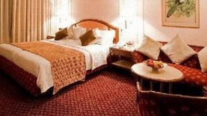 A hotel room with a large bed, a bedside table, a chair, and a small table with a vase. - Regent Hotel Andheri (Mumbai)